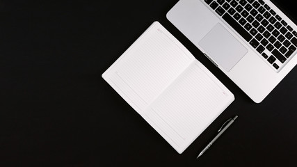 Modern minimalistic workspace with laptop, opened black leather notebook and pen on the black desk. Flat lay, copy space, top view