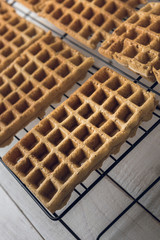 Belgian waffles on a black metal rack over a white rustic wooden table. Selective focus