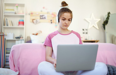 Young girl with laptop sitting on floor, relaxing during quarantine.