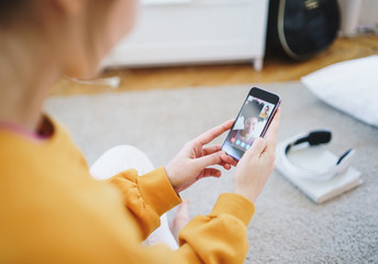 Unrecognizable young girl with smartphone sitting at home, making video call.
