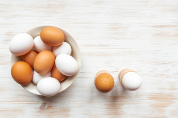 Free-range organic brown and white eggs in bowl and boiled eggs in holders on wood background with copy space