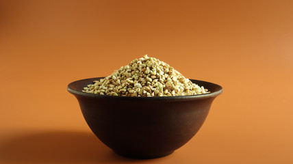 Raw green buckwheat in a brown clay plate on a brown background. Vegan organic food concept. The concept of diet, weight loss, healthy and proper nutrition. Copy space for text or logo.