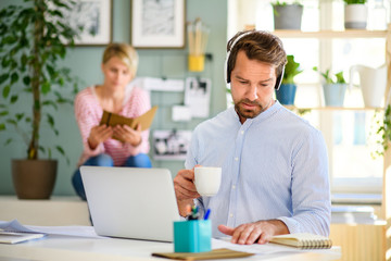 Mature businessman with headphones and laptop indoors in home office, working.