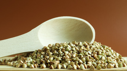 Buckwheat scattered background, raw green cereal in a wooden spoon. Healthy groats. Organic raw...