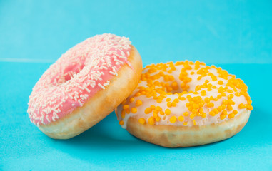 two donuts with, white-yellow-pink glaze, on a blue background, sweet dessert festive