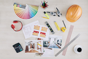 Table of professional architect with photos of interior vizualization, house blueprint, hardhat and color palette