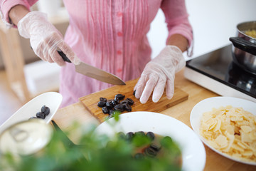 Unrecognizable woman with gloves cooking in kitchen indoors.