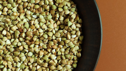 Raw green buckwheat in a brown clay plate on a brown background. Vegan organic food concept. The concept of diet, weight loss, healthy and proper nutrition. Copy space for text. Top view, flat lay.