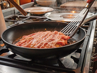 A chef cooks traditional okonomiyaki pancakes in a hot oil in a pan. The Japanese pancake mixture is turned over to see the golden underside.