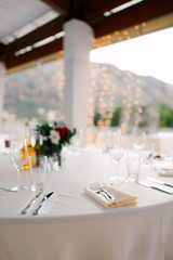 Close-up of a wedding dinner table - forks lie on a napkin. Table in background of the garland, on the table are glasses for wine and glasses, floral composition and carafe with olive oil