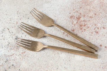 Three old bronze forks on concrete background.