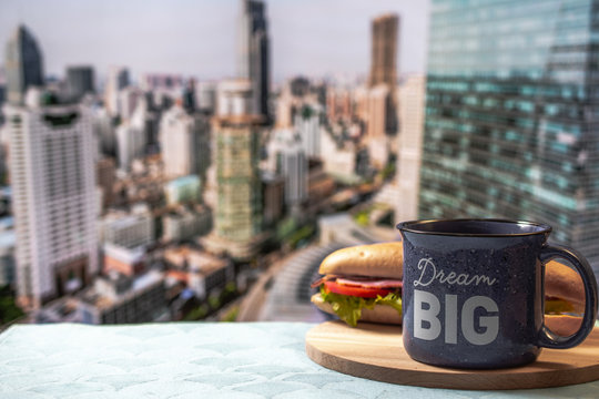 A cup of black coffee or tea and sandwich against the background of a blurry panorama of the city. Dream big concept. Life style