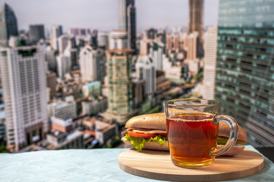 A cup of tea and sandwich against the background of a blurry panorama of the city. Dream big concept. Life style