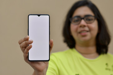 Young woman standing against a yellow wall showing her blank mobile phone white screen which can be used for copy space. Concept  Advertisement for App or promotion