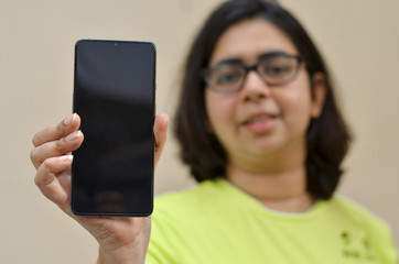Young woman standing against a yellow wall showing her blank mobile phone black screen which can be used for copy space. Concept  Advertisement for App or promotion