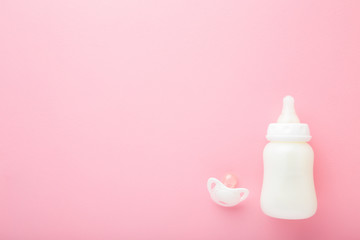 Bottle of white milk and soother on light pink table background. Baby feeding concept. Pastel...