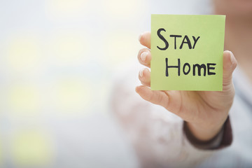 Hand holding sticky note with Stay Home text