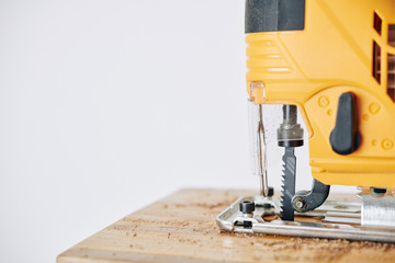 Close-up image of professional electric jigsaw cutting wooden block in workshop