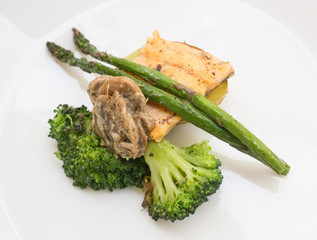 dish of fried river trout fillet with a complex side dish of broccoli, asparagus sprouts and mushroom sauce on white background