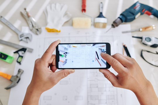 Hands of construction engineer photographing house blueprint on smartphone to send photo to colleague or client