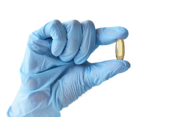 A hand in blue glove hold a capsule with fish oil, omega-3. Healthcare and medical concept.