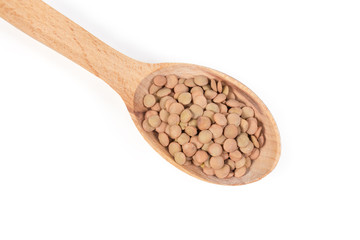 Uncooked brown lentil in wooden spoon, top view close-up
