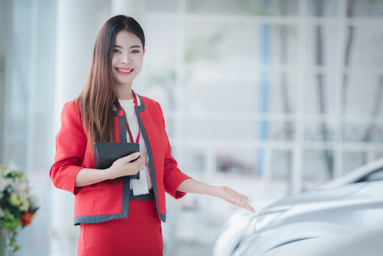 A beautiful Asian car saleswoman is happy to sell a new car in the showroom and enjoy selling the car.