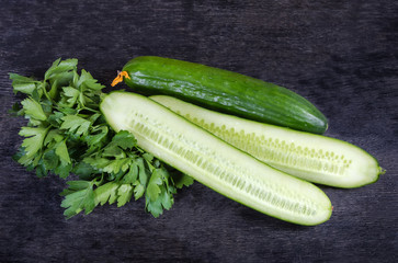 Whole and halves cucumbers with parsley on the black surface