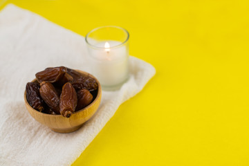 Ramadan Kareem Festival. Close up of dried dates fruit in wooden bowl with candle on yellow background. Copy space