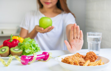 Close up of young Asian woman using hand push out her favourite fried chicken, french fries and choose green apple, fruit and vegetables for good health. Woman on dieting concept. Close up