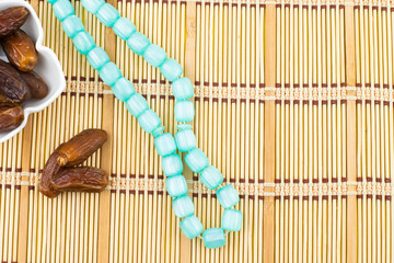 Ramadan Kareem Festival. Close up of dried dates fruit in bowl with blue rosary on wooden background. Copy space