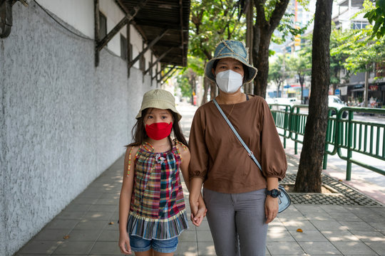 Portrait photo of Asian mother and her daughter wearing medical face mask while walking in the city.