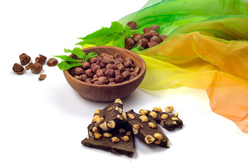 Hazelnuts in wooden bowl, green leaves and craft chocolate isolated on white background