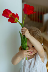 little blonde girl in a white dress holds a bouquet of red tulips in her hands