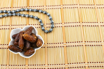 Ramadan Kareem Festival. Close up of dried dates fruit in bowl with black rosary on wooden background. Copy space