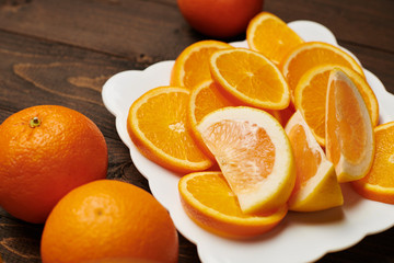 Fresh orange fruits whole and sliced on a plate, dark wooden background - natural and healthy food.