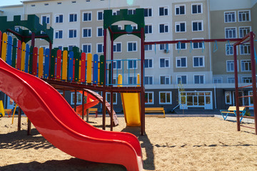 Fototapeta na wymiar Urban residential infrastructure without people - children's playground next to a condominium. Swing, slide, stairs, multistory building. A place for children to play.