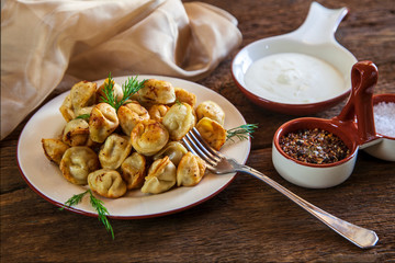Dumplings with meat, onion and sour cream, on a plate, on wooden background