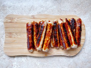 Closeup view of fried British Cumberland sausages on a wooden chopping board in the kitchen. Preparing breakfast at home with cooked meat. Traditional English pork breakfast.