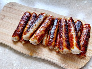 Closeup view of fried British Cumberland sausages on a wooden chopping board in the kitchen. Preparing breakfast at home with cooked meat. Traditional English pork breakfast.