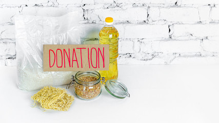 Banner. Food collection for donations, on a white brick background. Anti-crisis stock of essential goods for the period of quarantine isolation. Food delivery, coronavirus. The shortage of food.