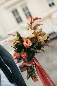 Beautiful winter bouquet in the hands of the groom. Groom holding bride's bouquet. dridal bouquet of roses with pine, branches of eucalyptus, succulents and pine cone in man's hands