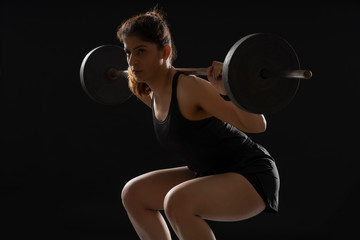 Woman working out with barbell in front of a dark background. 
