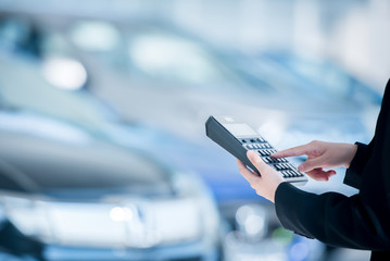 Car salesmen are using calculators to calculate the new car prices in the showroom and calculate...