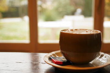 Hot coffee mug and chocolate cube on a table in the background a window leading to the courtyard