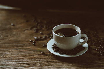 Hot black coffee cup and coffee beans on wooden background with natural light in the morning