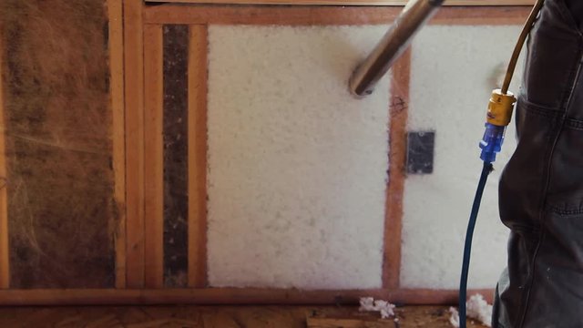 A worker fills in a small space with blown-in insulation