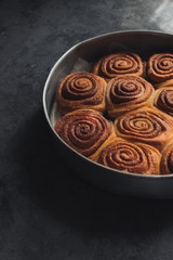 Delicious homemade cinnamon rolls bun in circle shaped baking tray on the dark grey concrete background. Vertical image