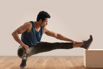 Man stretching his legs over a block in front of a plain background. 
