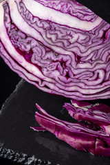 Obraz premium Top view of open red cabbage, with pieces, on wet black slate and black background, vertical